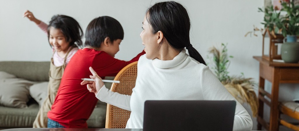 woman sitting at her laptop with her children behind her